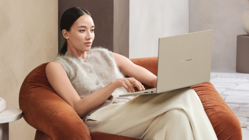 A woman sitting on a couch and using the Asus Zenbook A16